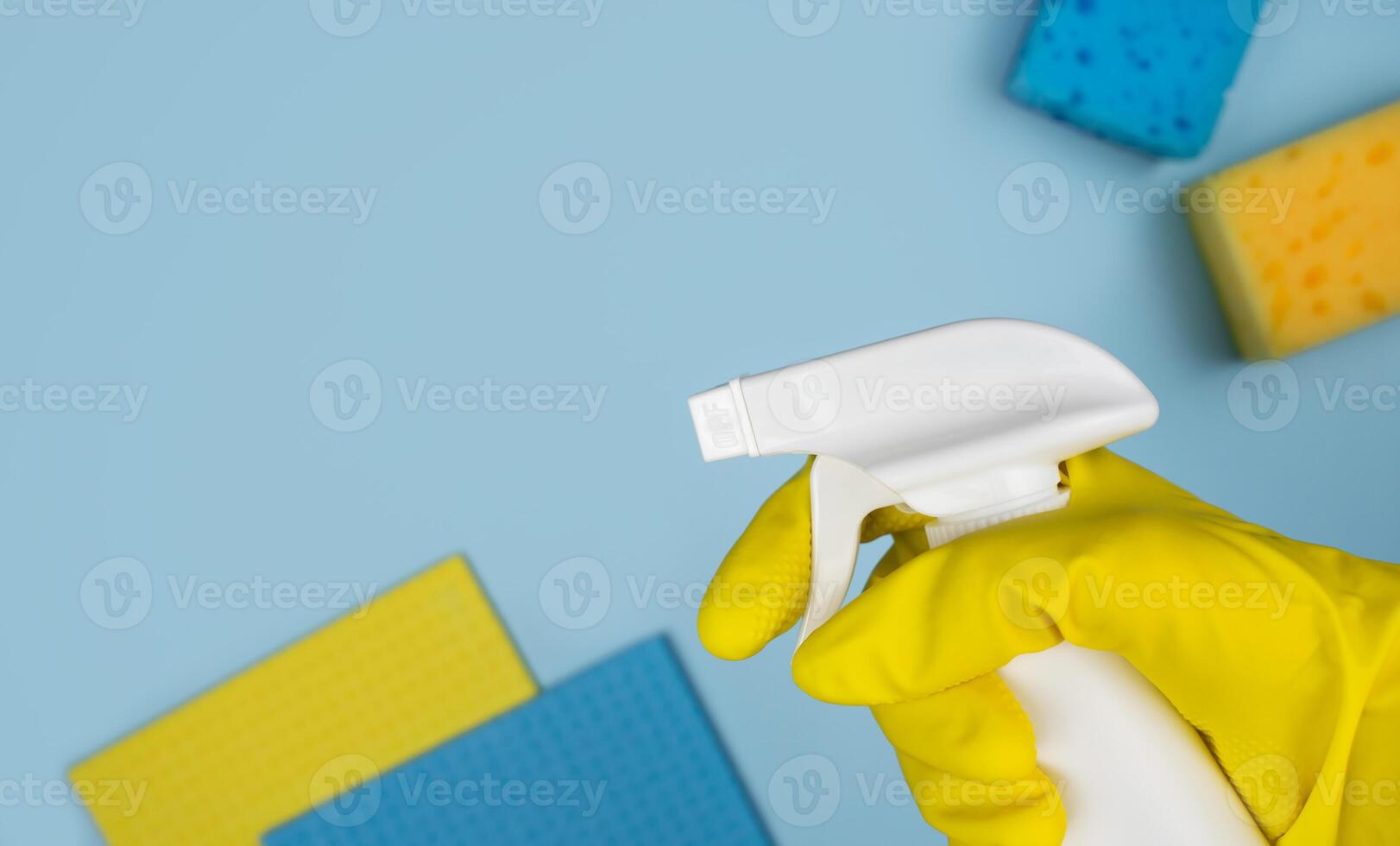 A woman's hand in a rubber glove holds a spray cleaner against the background of various cleaning items. Banner. Top view. Place for text. photo