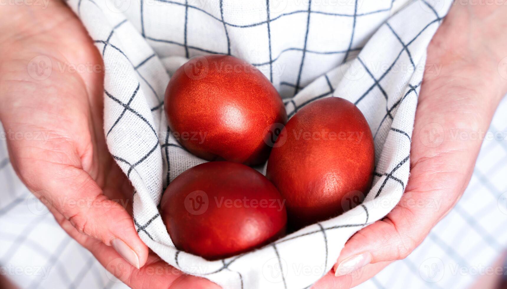 Woman's hands hold colored red Easter eggs in an apron. Coloring eggs for Easter. Christian traditions. Close-up. Selective focus. photo