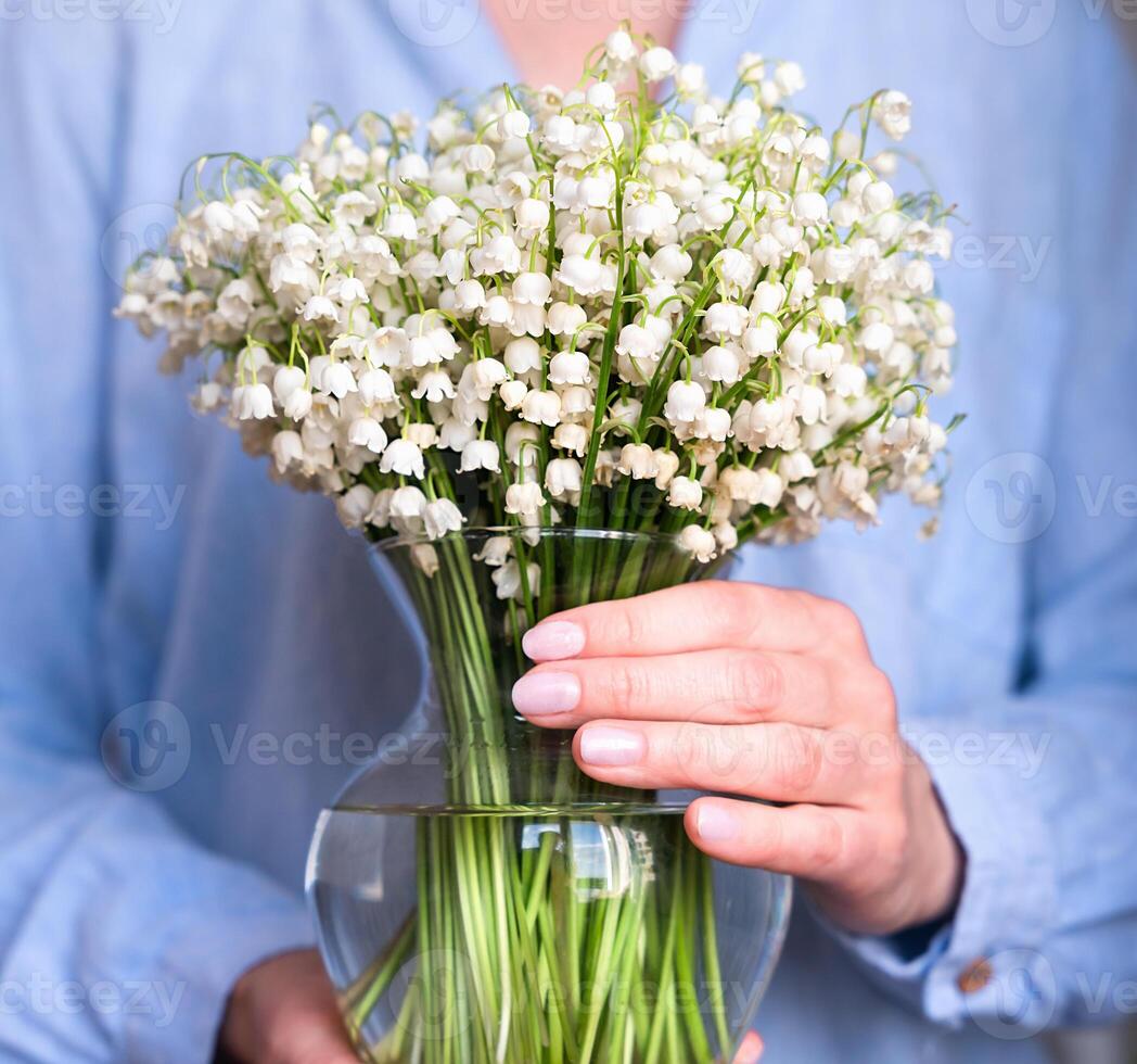 A young woman holds a vase with lilies of the valley. Spring mood. Close-up. Selective focus. photo