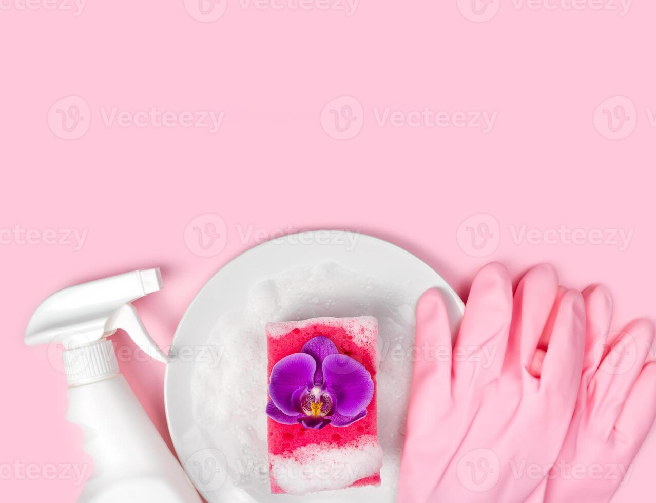 Detergent, kitchen sponge, pink rubber gloves, soapy plate and orchid flower on the pink background. Flatlay. Top view. Copy space. photo