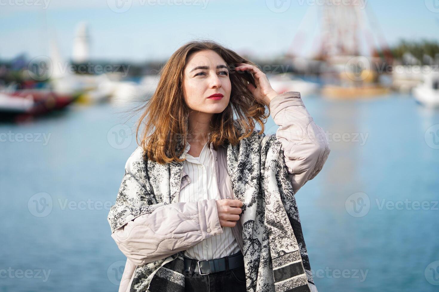 Beautiful girl standing near sea. Seaport or berth in background. Young woman Wearing casual photo