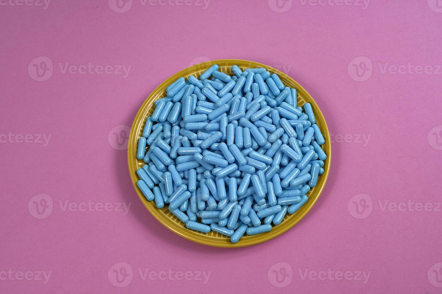 Yellow plate full of blue medicine capsules representing drug overdose photo