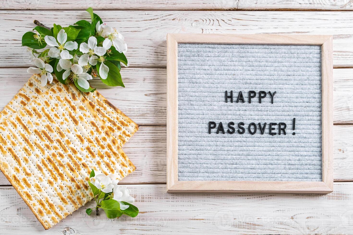 Happy Passover flatlay. Jewish matzo bread and flowers on white wooden background. photo