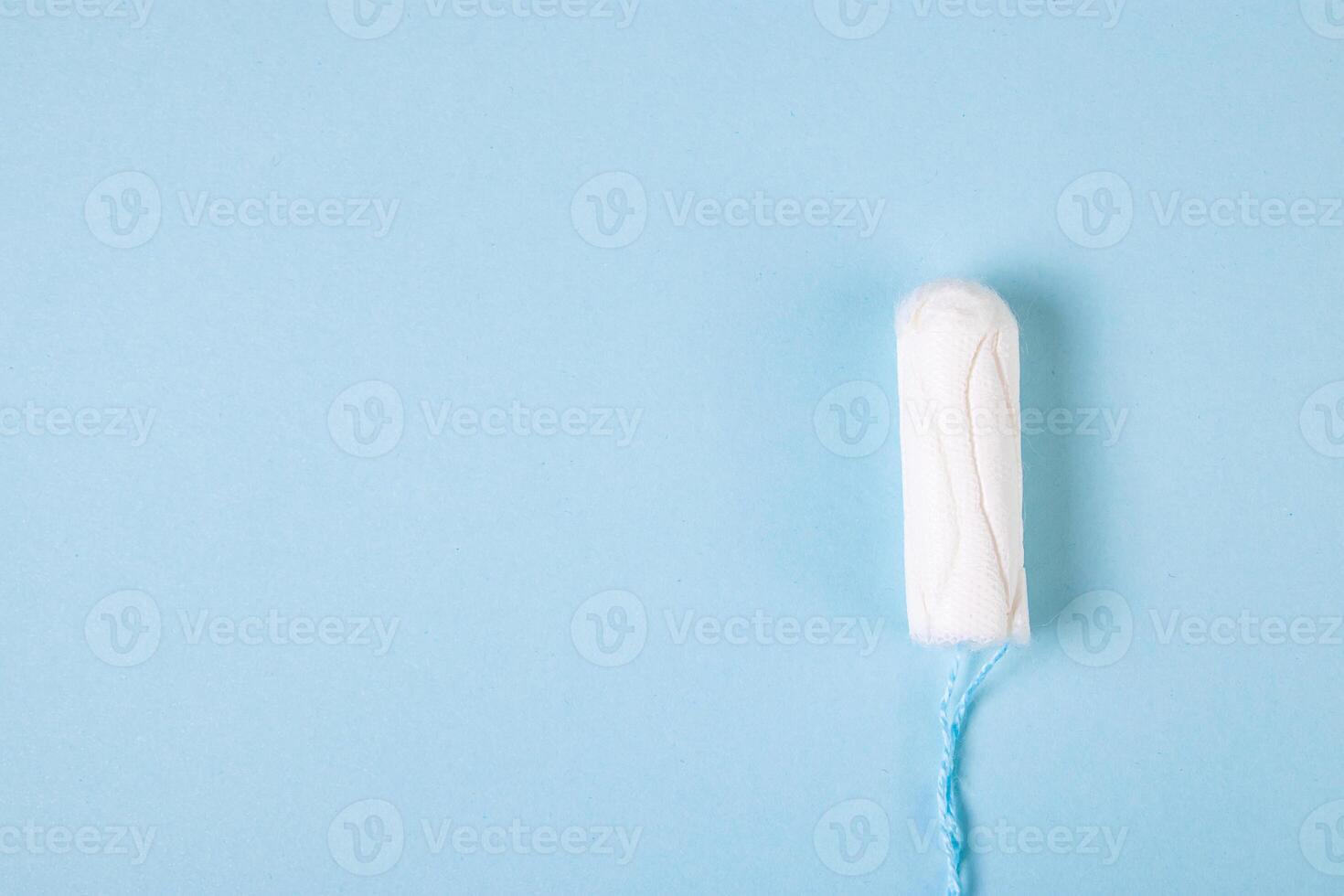 Hygienic cotton tampon on blue background. Feminine menstrual hygiene products. photo