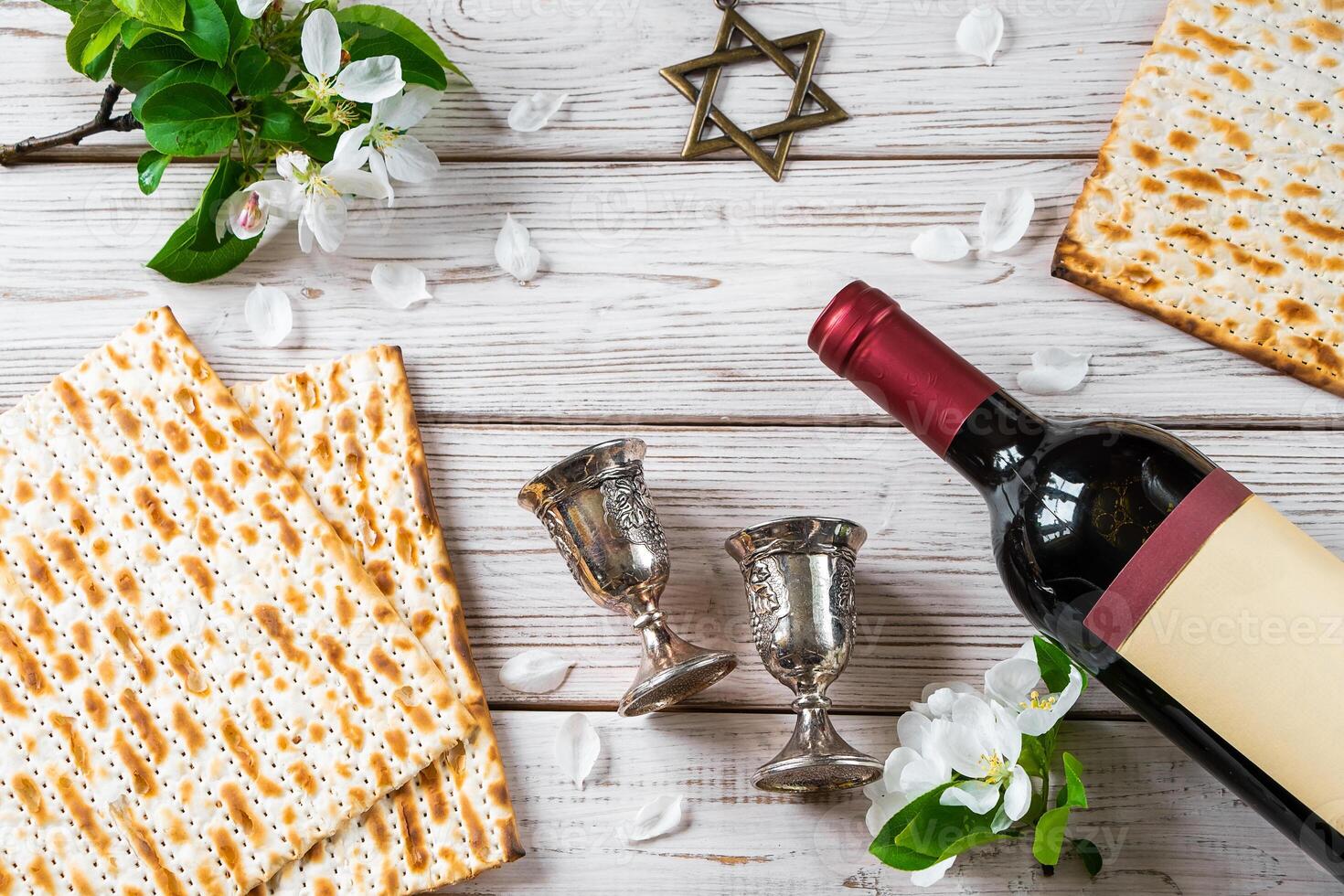 Jewish religious holiday of Passover. Bottle of wine, matzo and flowers on white wooden background. photo