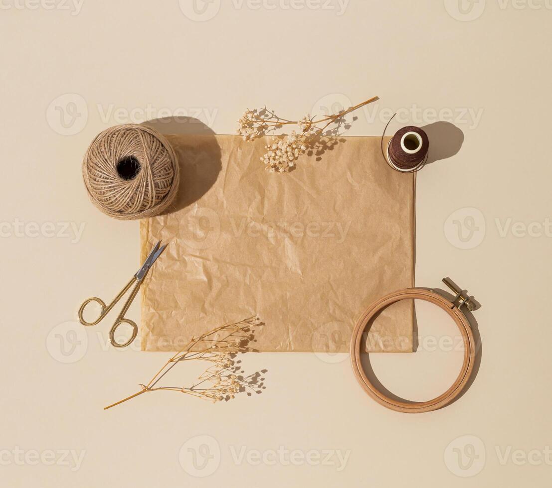 Creative vintage composition of sewing scissors, thread, jute, embroidery hoop, dry flowers and old crumpled paper card note copy space on beige background. Minimal handmade sewing accessories concept photo