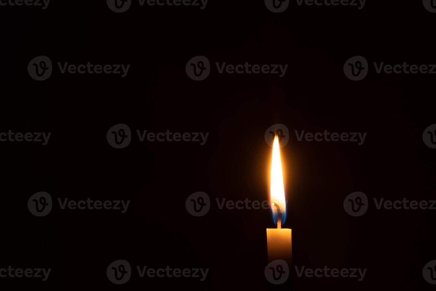 Single burning candle flame or light glowing on an orange candle on black or dark background on table in church for Christmas, funeral or memorial service with copy space photo