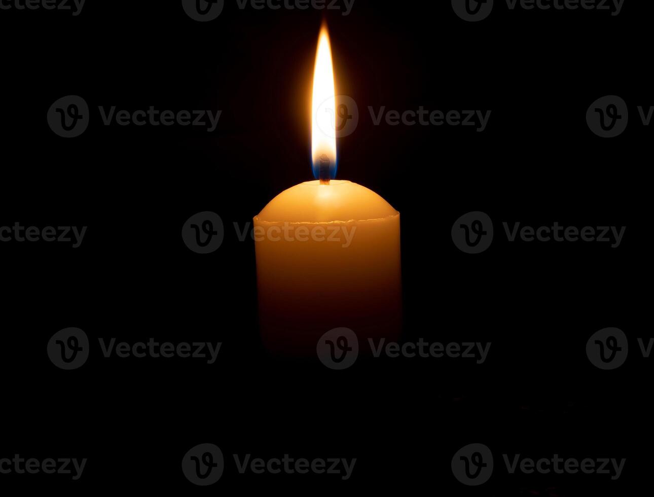 Single burning candle flame or light glowing on big white candle on black or dark background on table in church for Christmas, funeral or memorial service with copy space photo