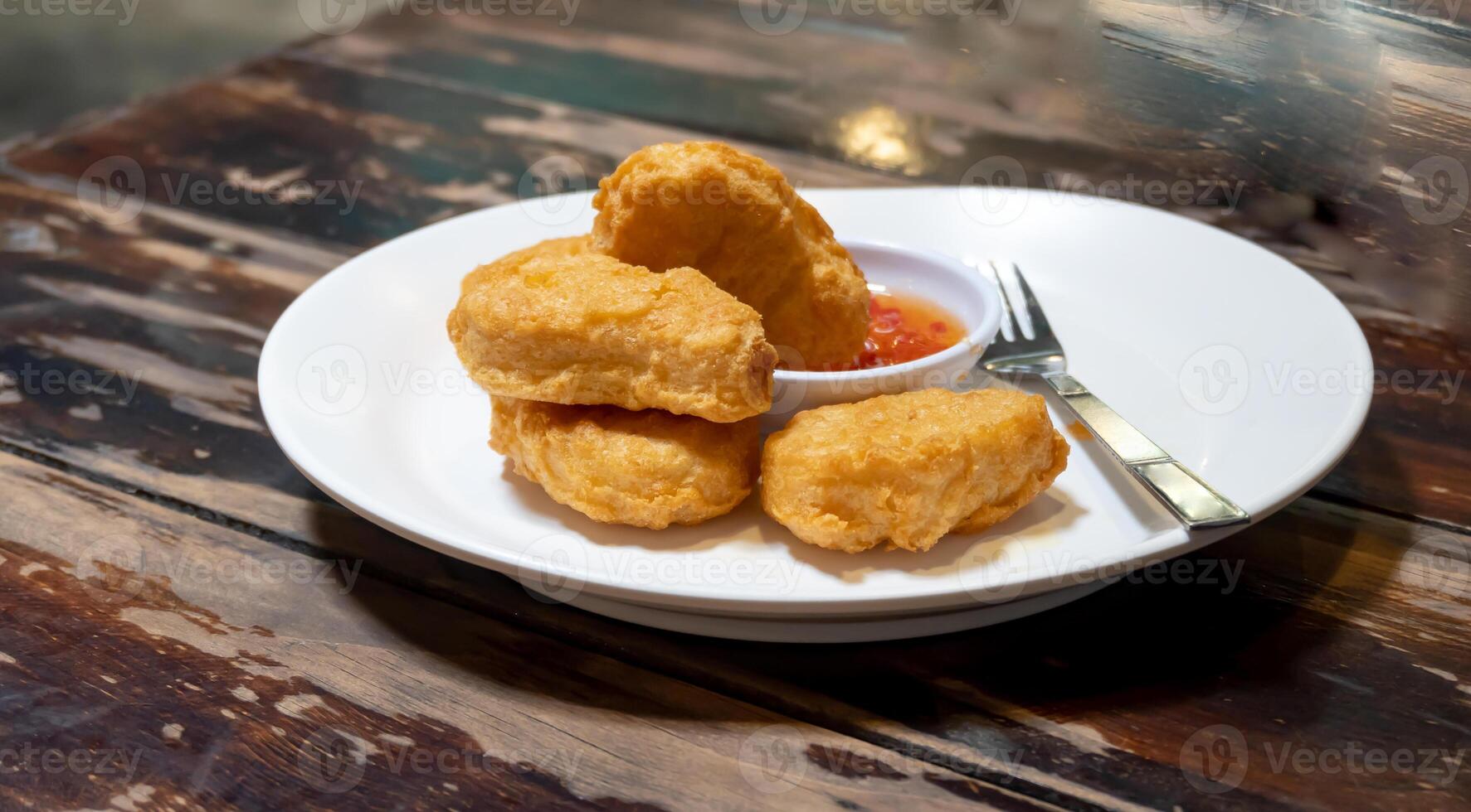 Front view of chicken nuggets with chili sauce in white plate on brown wooden table photo