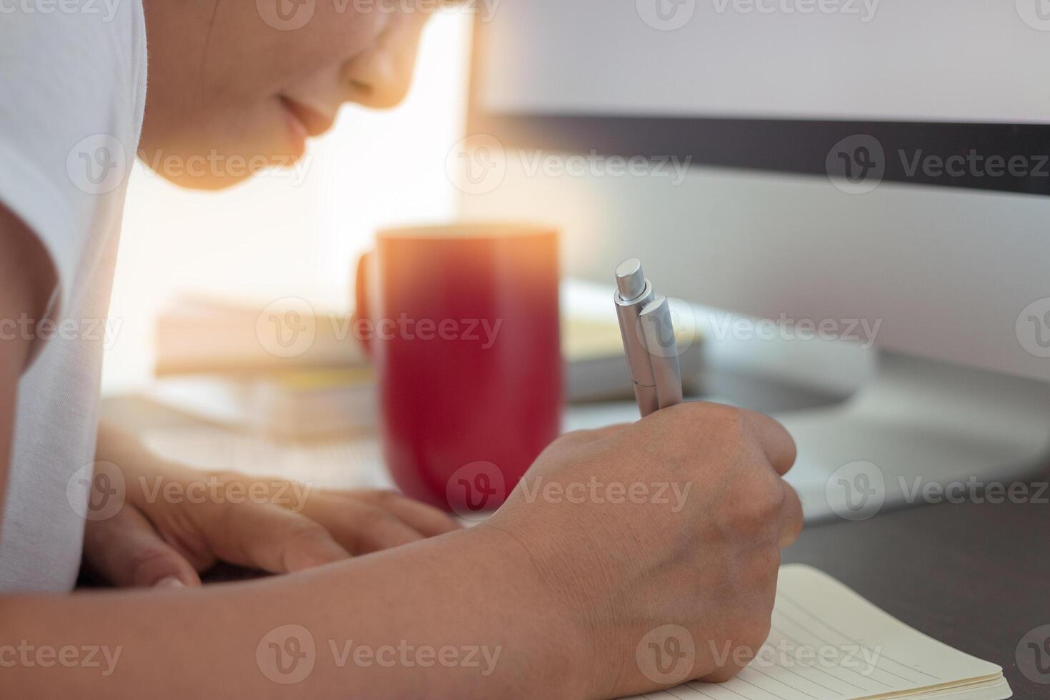 Women working on the desk and desktop computer, notebook, red coffee mug photo