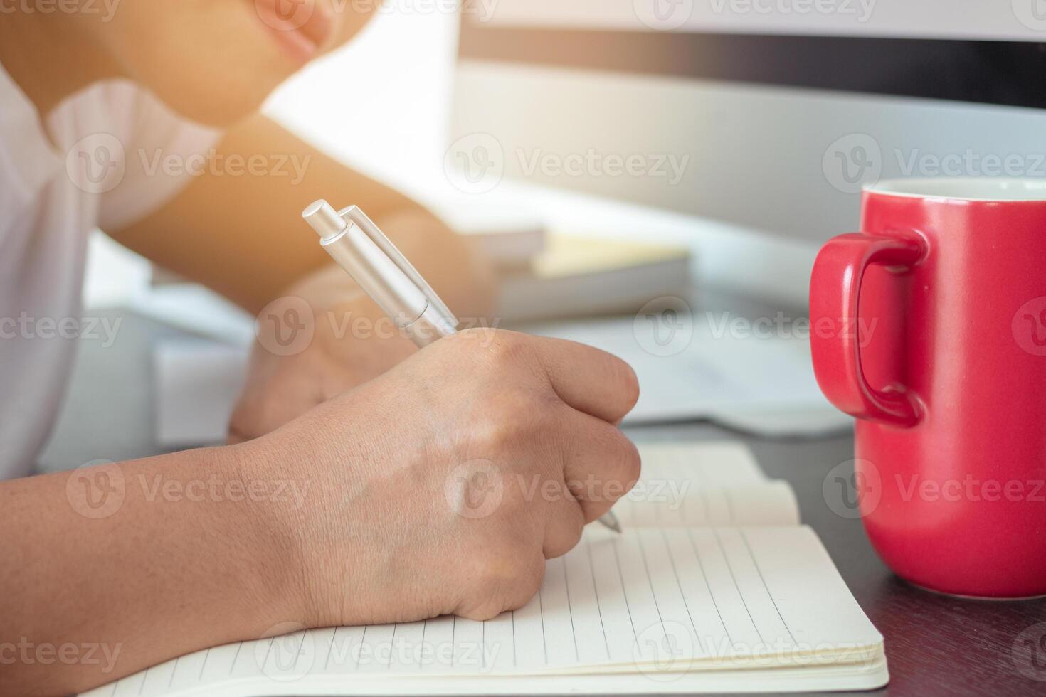Women working on the desk and desktop computer, notebook, red coffee mug photo