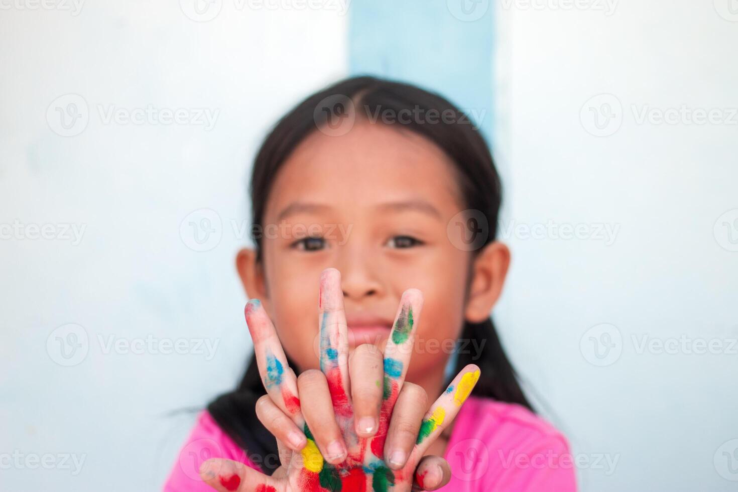 Cute little girl with colorful painted hands on wall background photo