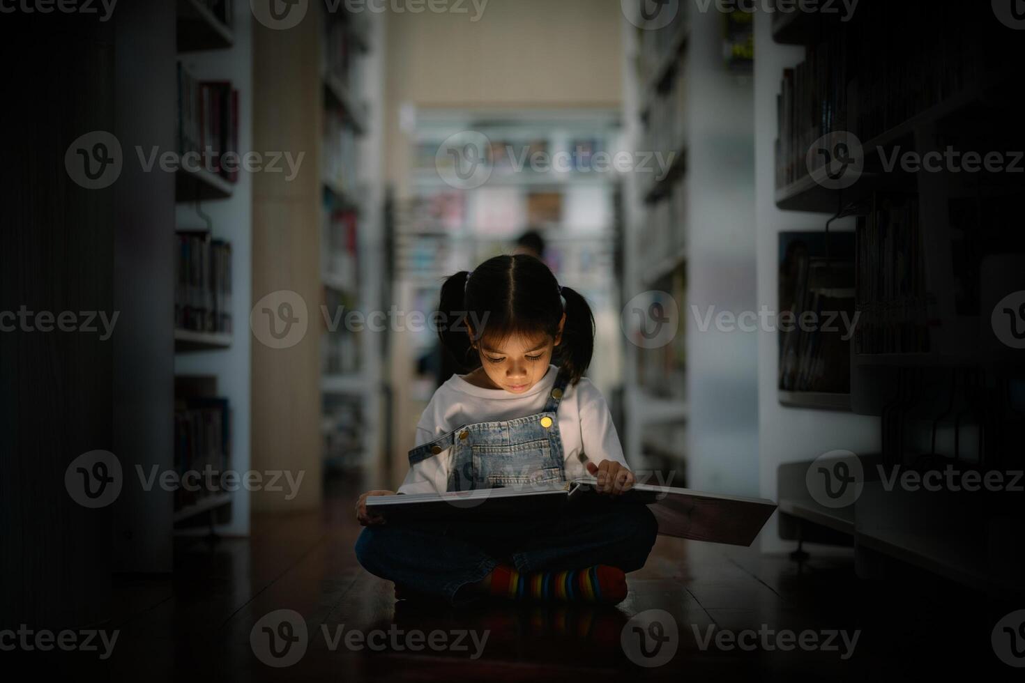 A young girl is sitting on the floor in a library, reading a book photo