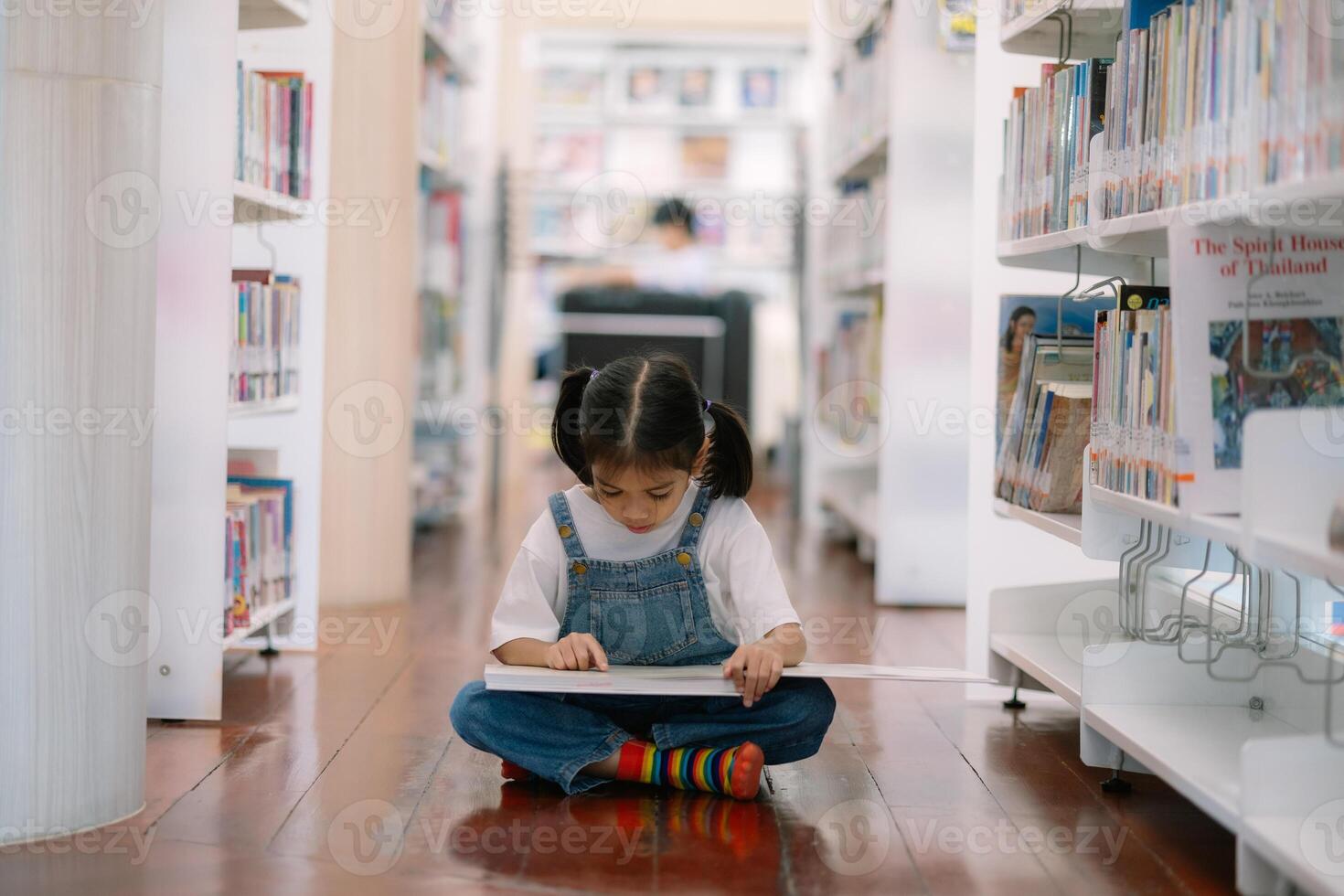 A young girl is sitting on the floor in a library, reading a book photo