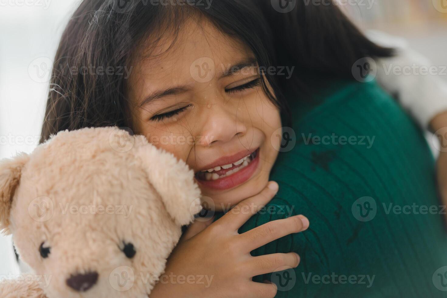 A young girl is hugging a teddy bear while crying photo