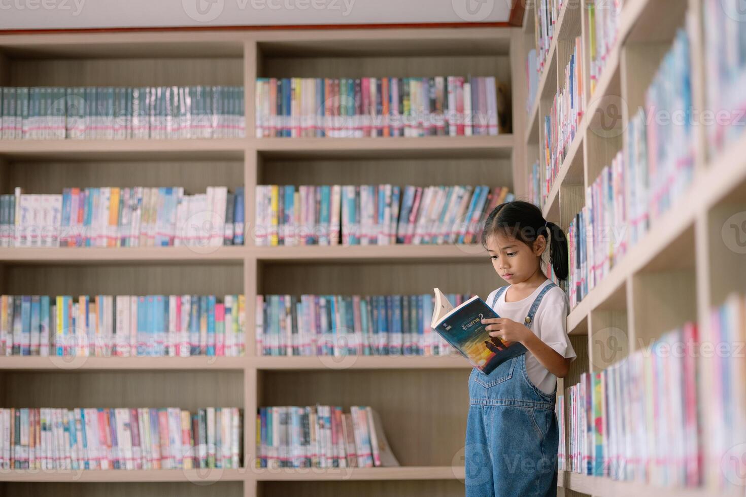 A young girl is reading a book in a library photo