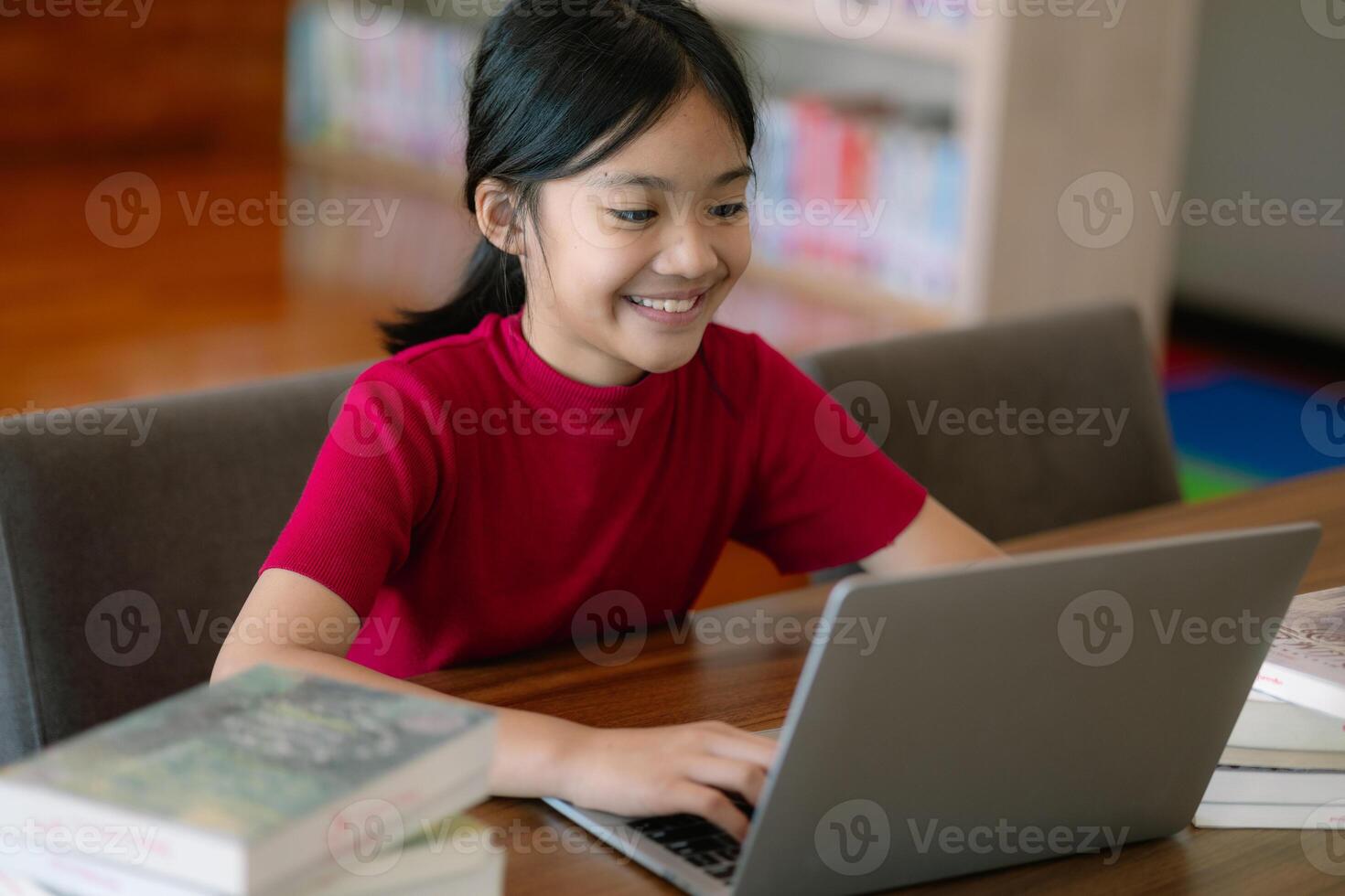 A young girl is sitting at a table with a laptop and several books photo