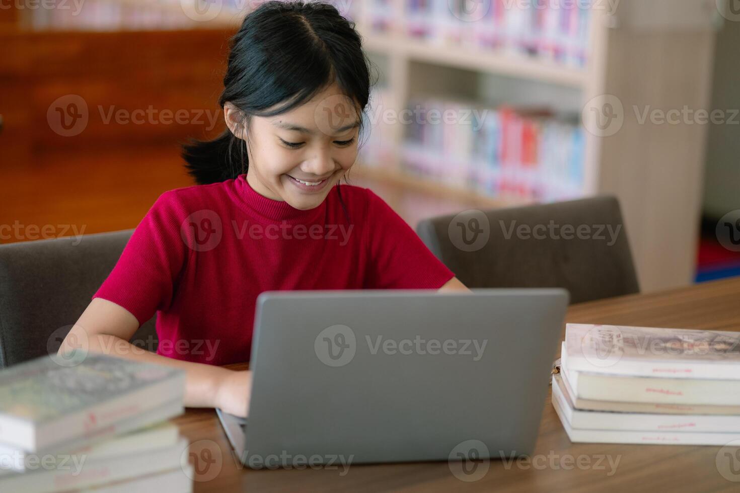 A young girl is sitting at a table with a laptop and a stack of books photo