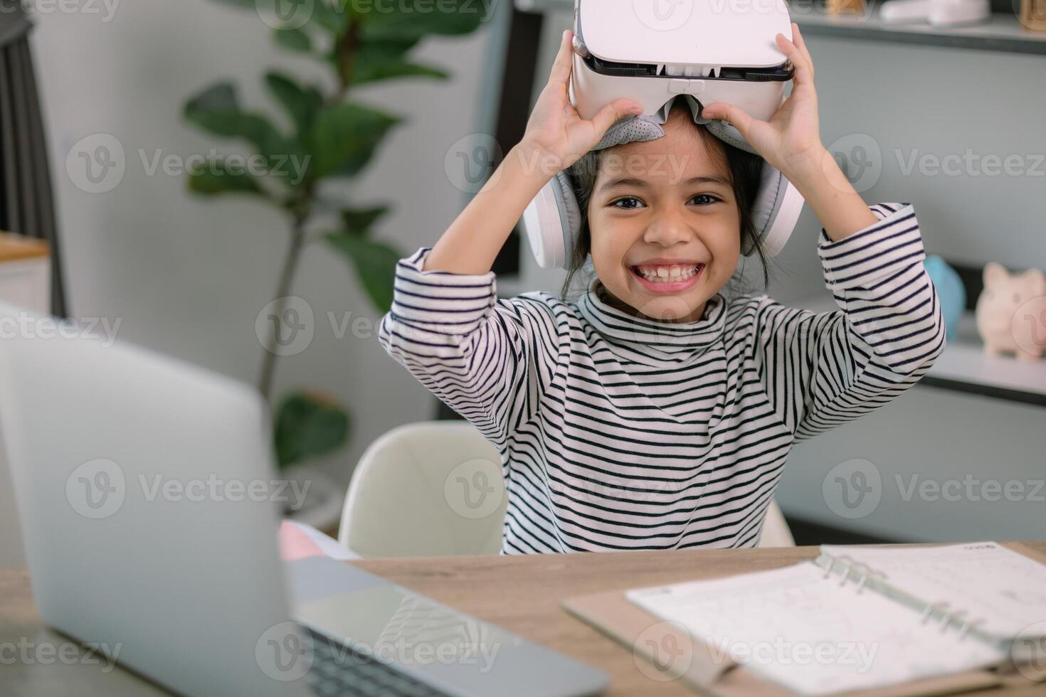 linda asiático pequeño niña vistiendo vr lentes con un ordenador portátil metido en el mesa en vástago tecnología clase. en línea educación. erudición. foto