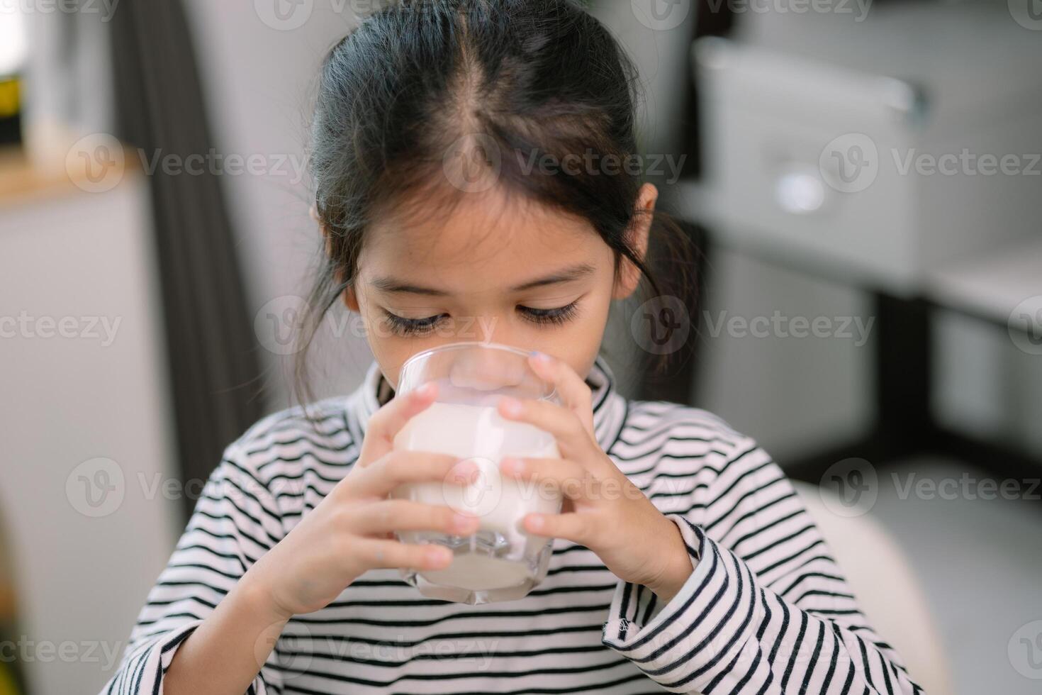 Asian Cute little girl drinking milk at the table at home. enjoys drinking milk. photo