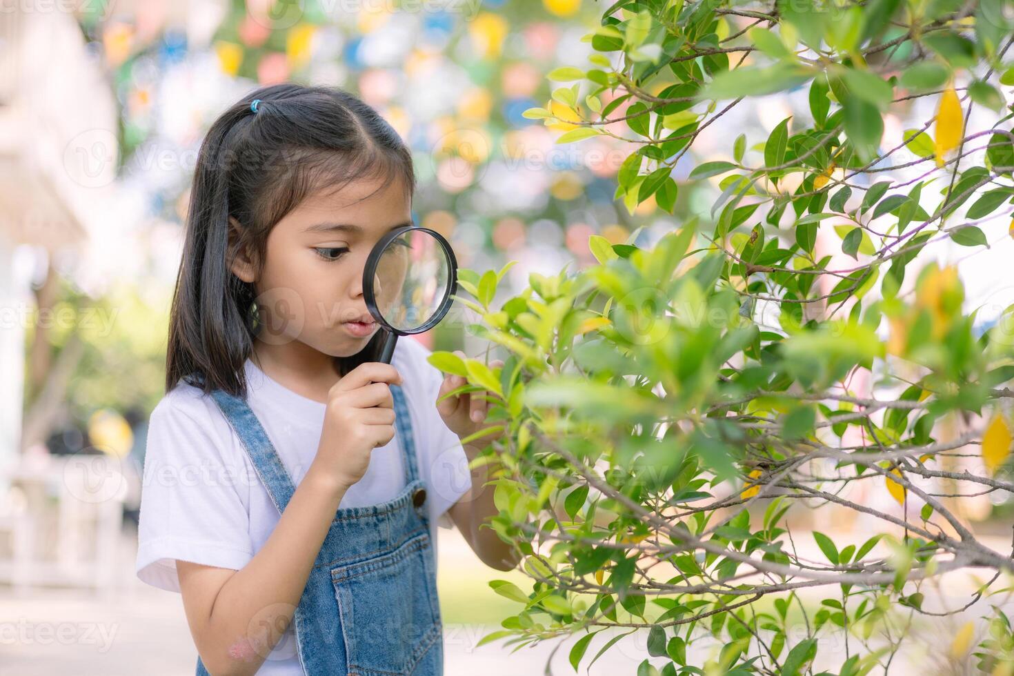 A young girl is looking through a magnifying glass at a leaf photo