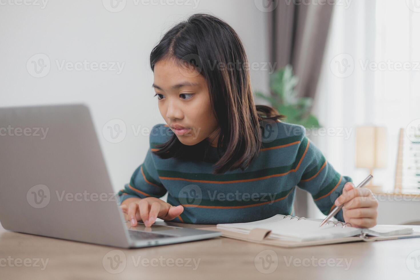 A girl is sitting at a desk with a laptop and a notebook photo