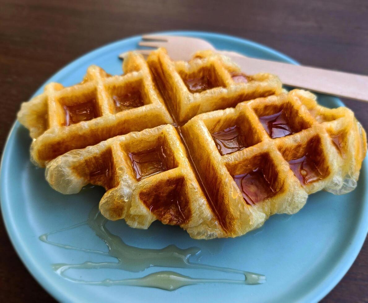 Closeup waffle topped with honey sauce on blue plate at cafe. Sweet bakery in dish on wooden table or background with copy space. photo