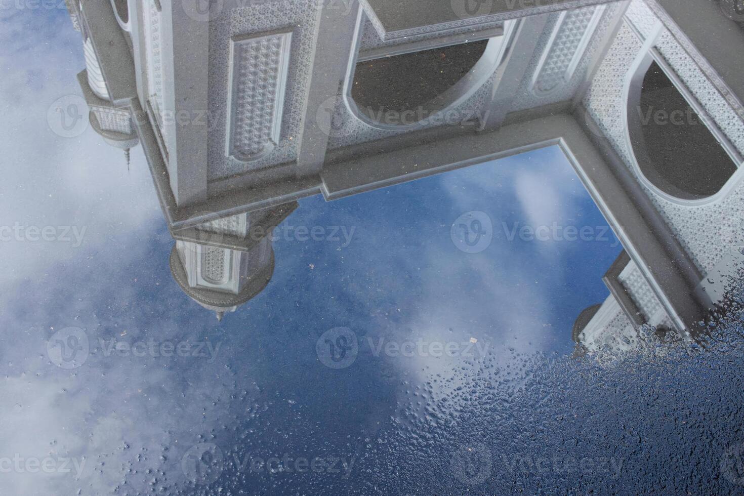 View of the White Mosque with water reflections on the road against a blue sky background photo