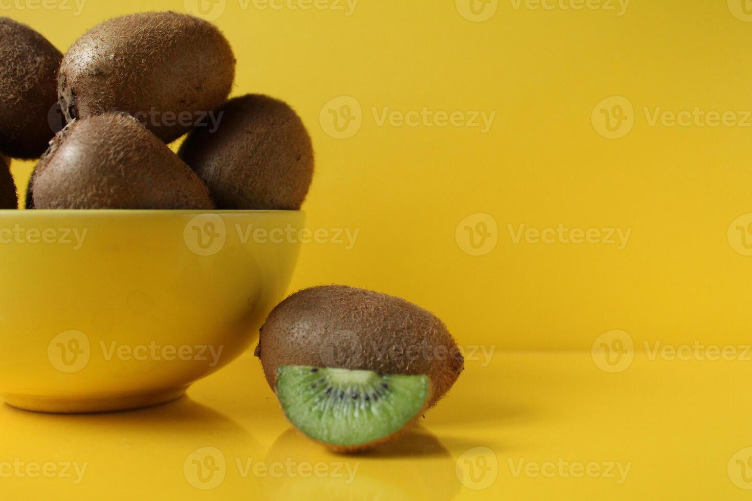 Still life of fruit trending illuminatiited yellow kiwi in a bowl plate of yellow and next pieces of kiwi yellow background with a place to text copyspace photo