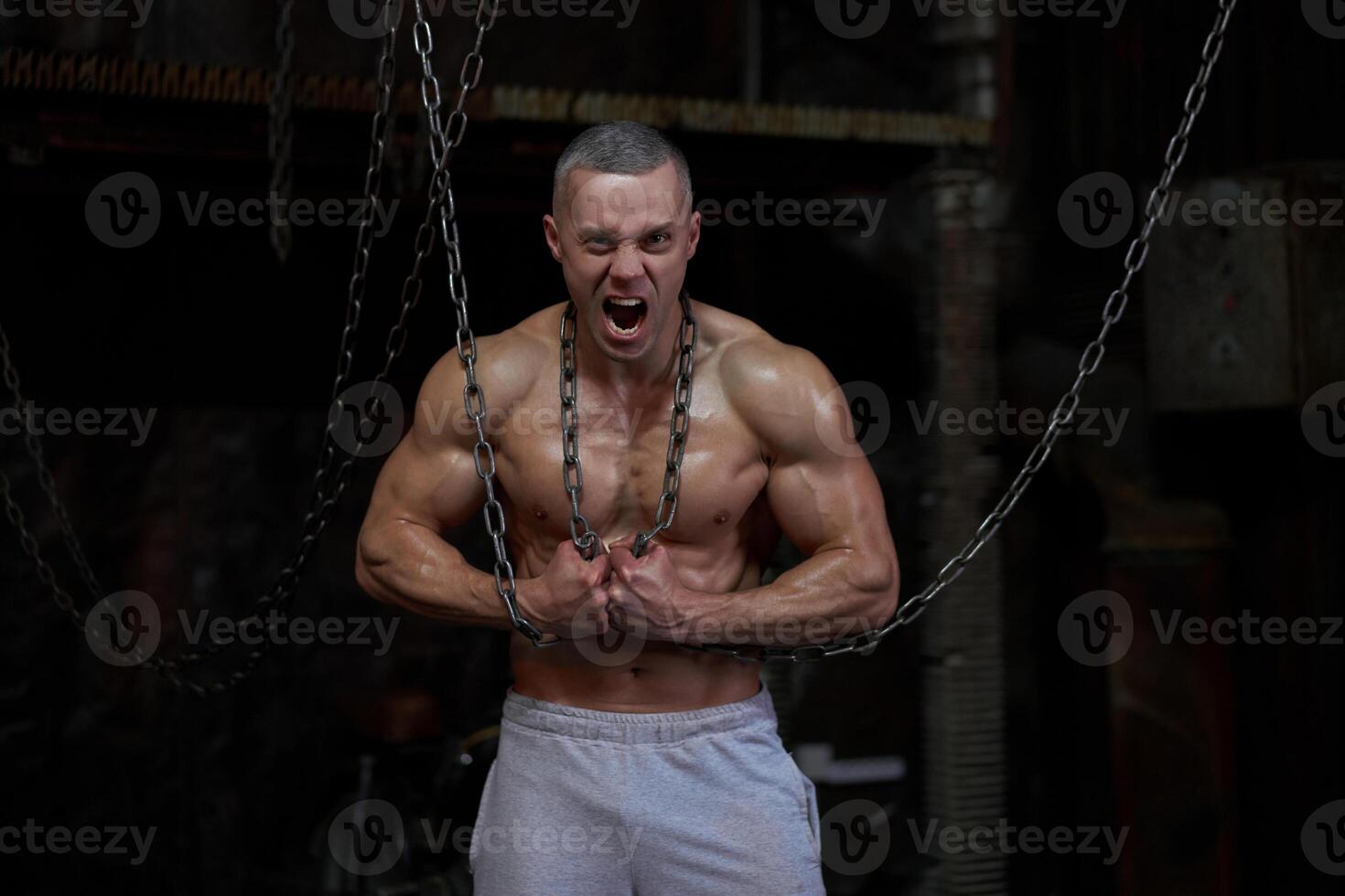 Primal instinct. Angry muscular man screaming at camera and breaking chains on chest photo