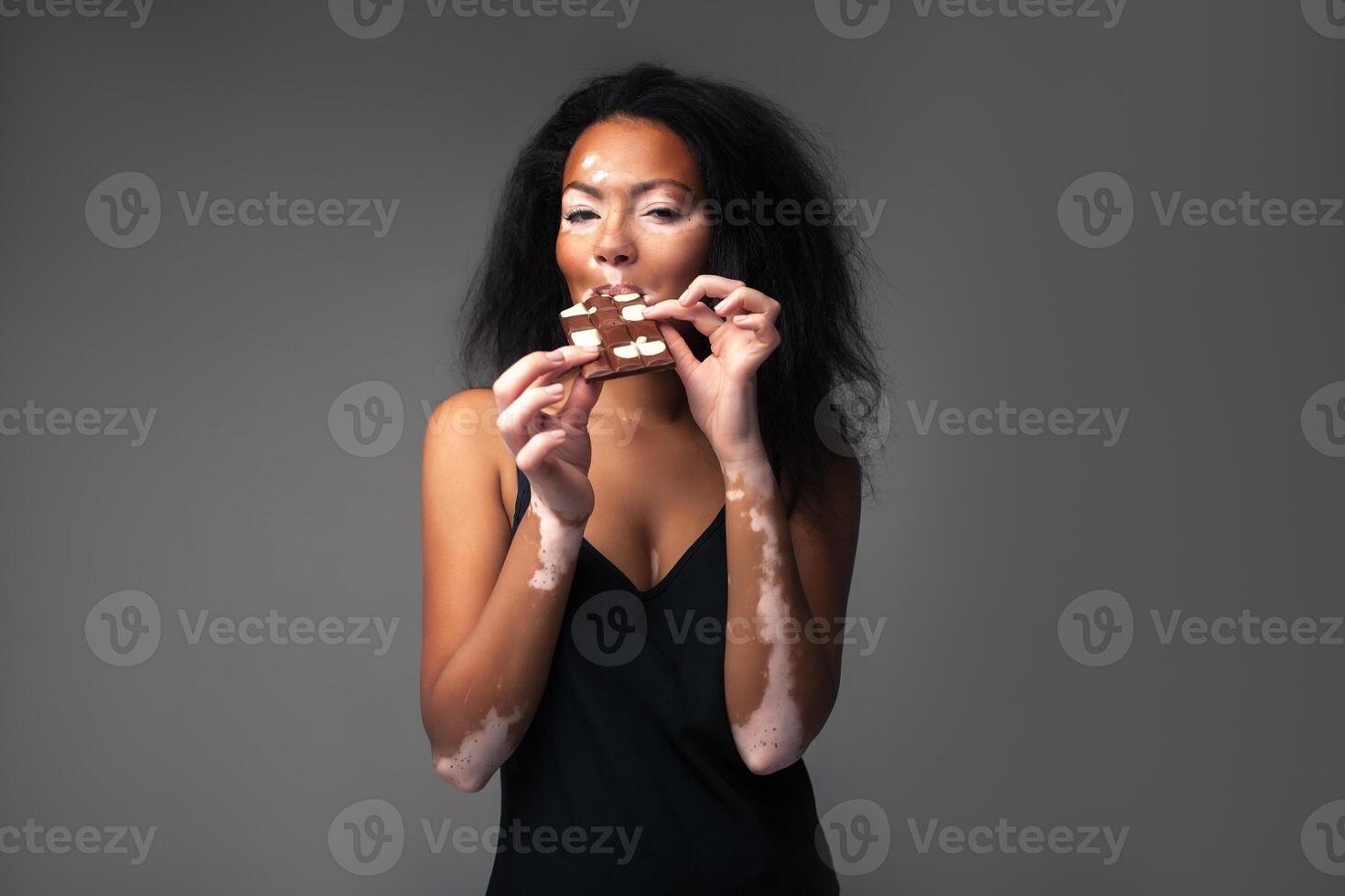 beautiful African girl with vitiligo in the studio eating black and white chocolate. photo