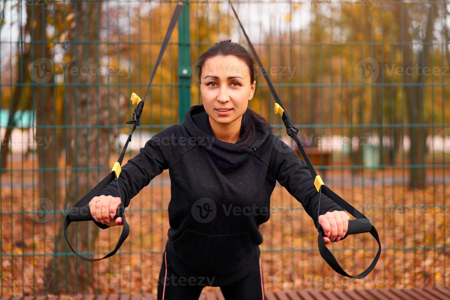 Girl athlete functional training on sportground. Mixed race young adult woman do workout with suspension system. Healthy lifestyle. Stretching outdoors playground. photo