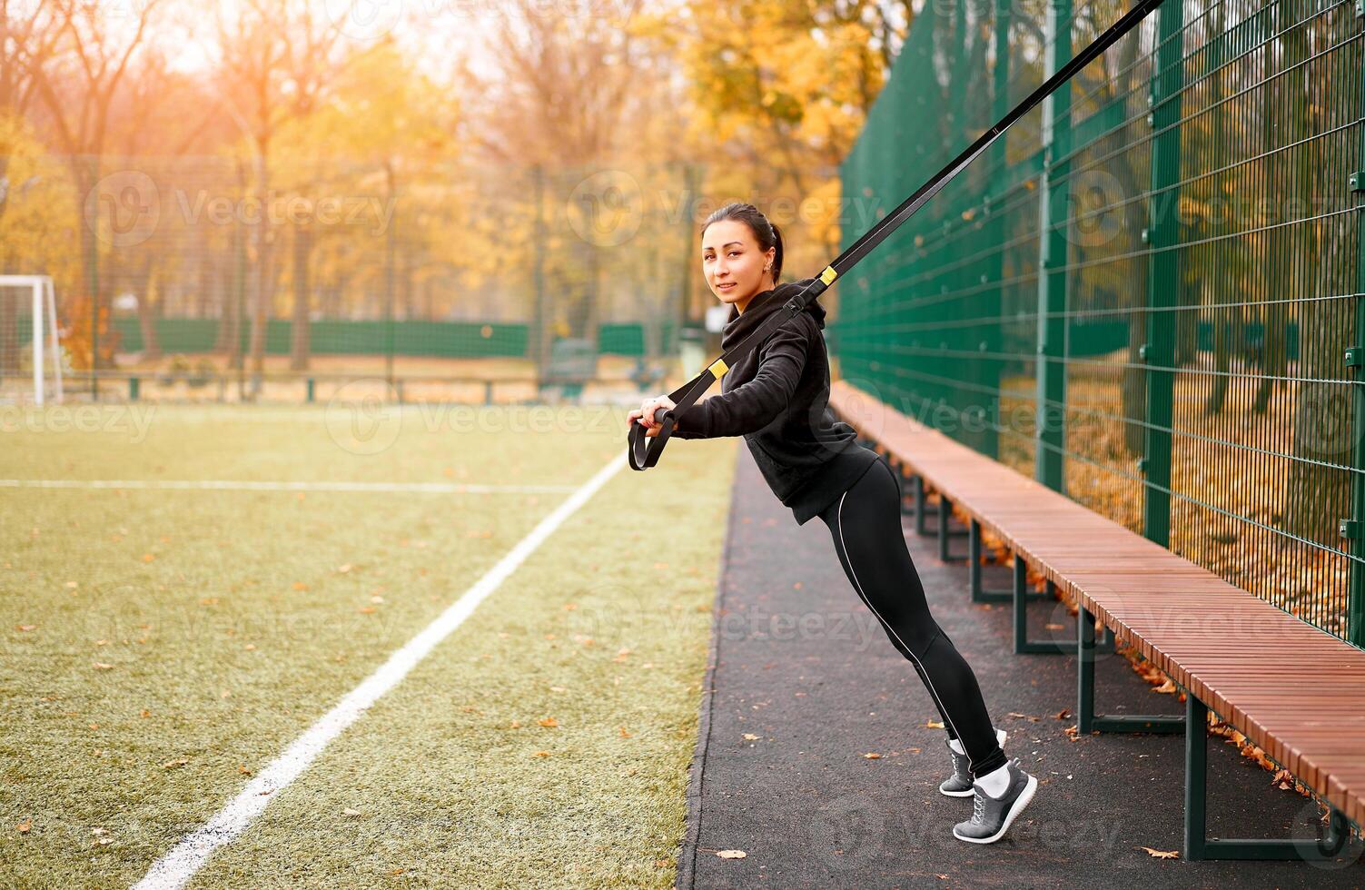 Girl athlete training using trx on sportground. Mixed race young adult woman do workout with suspension system. Healthy lifestyle. Stretching outdoors playground. photo