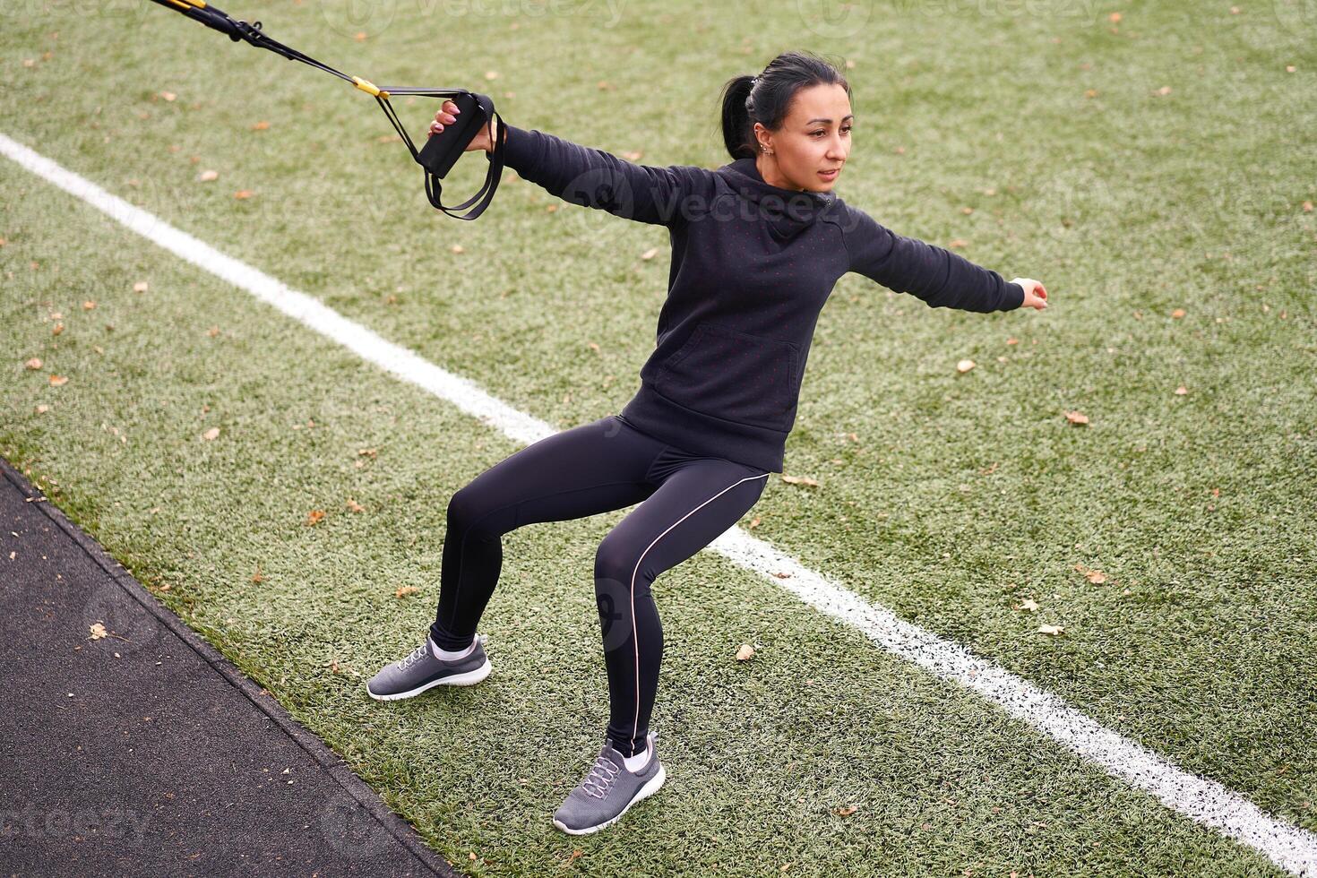 Girl athlete training using trx on sportground. Mixed race young adult woman do workout with suspension system. Healthy lifestyle. Stretching outdoors playground. photo