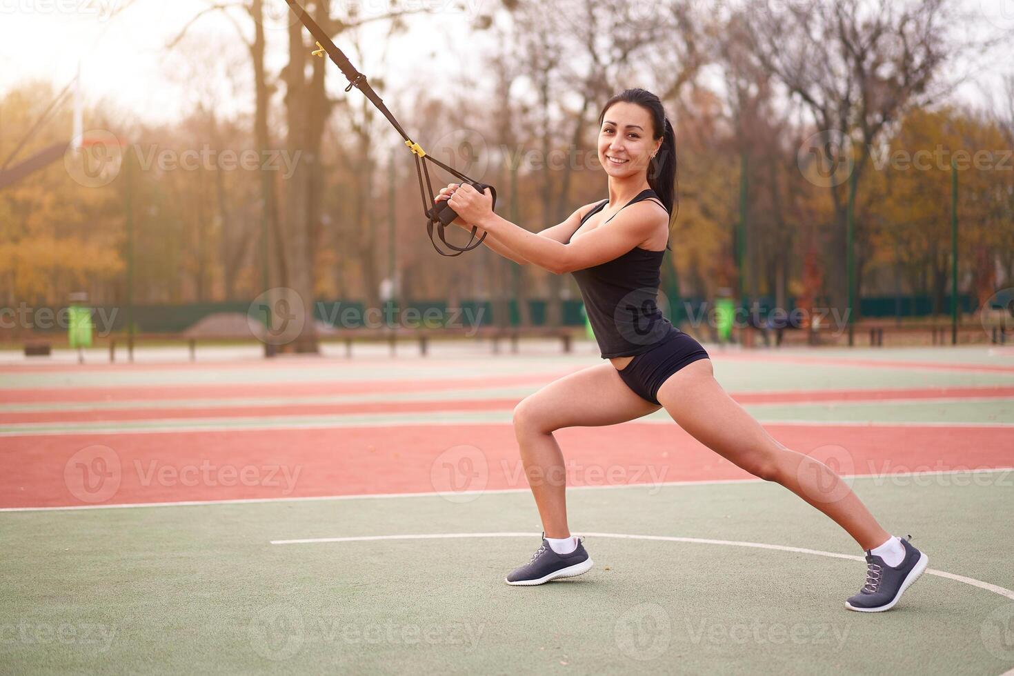 Girl athlete training using trx on sportground. Mixed race young adult woman do workout with suspension system. Healthy lifestyle. Stretching outdoors playground. photo