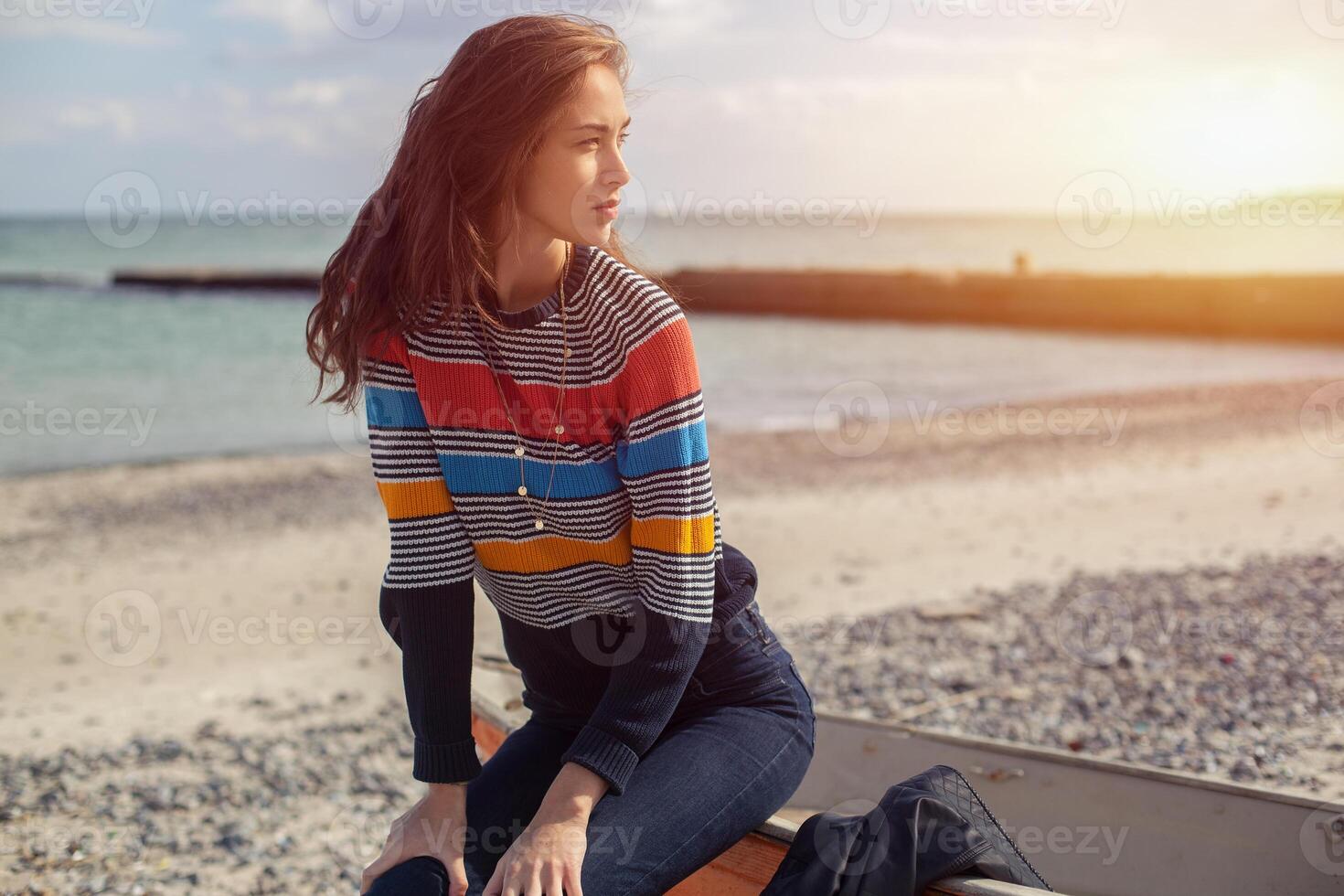 A girl sideways near a red boat on the beach by the sea photo