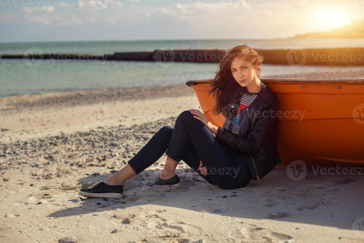 A girl sideways near a red boat on the beach by the sea photo