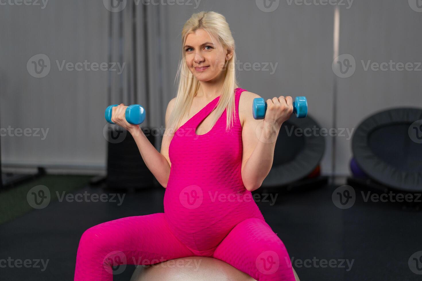 Pregnant woman exercise withdumbbells on fitness bal in gym photo