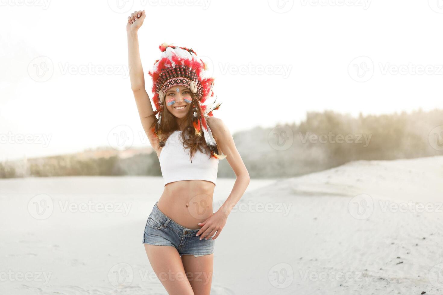 un hermosa joven caucásico niña en un blanco parte superior y mezclilla bermudas. en su cabeza vistiendo un indio sombrero cucaracha. en pie en el desierto. foto