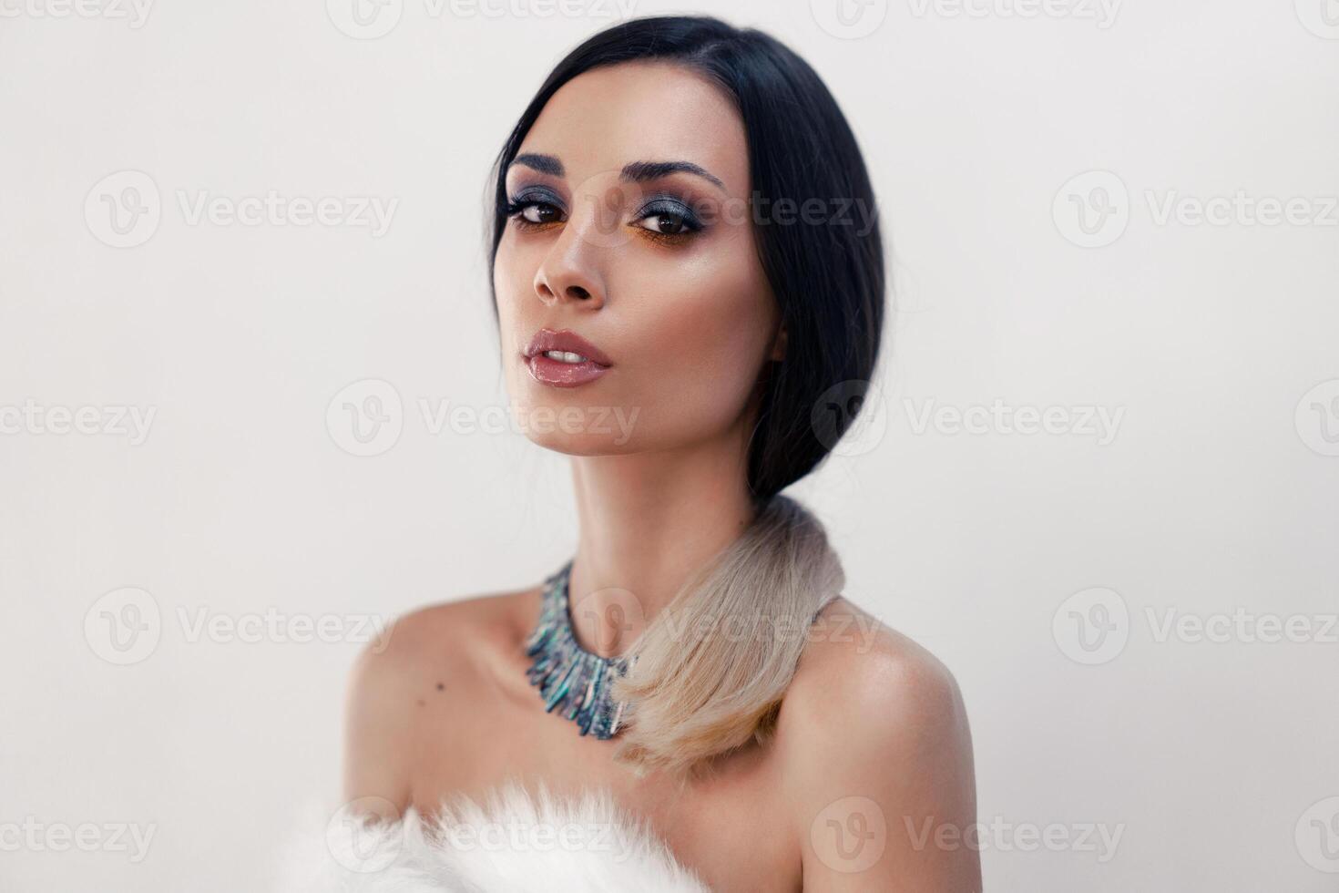 Portrait of a beautiful young Caucasian girl with bare shoulders and beautiful evening make-up dressed in artificial white fur photo