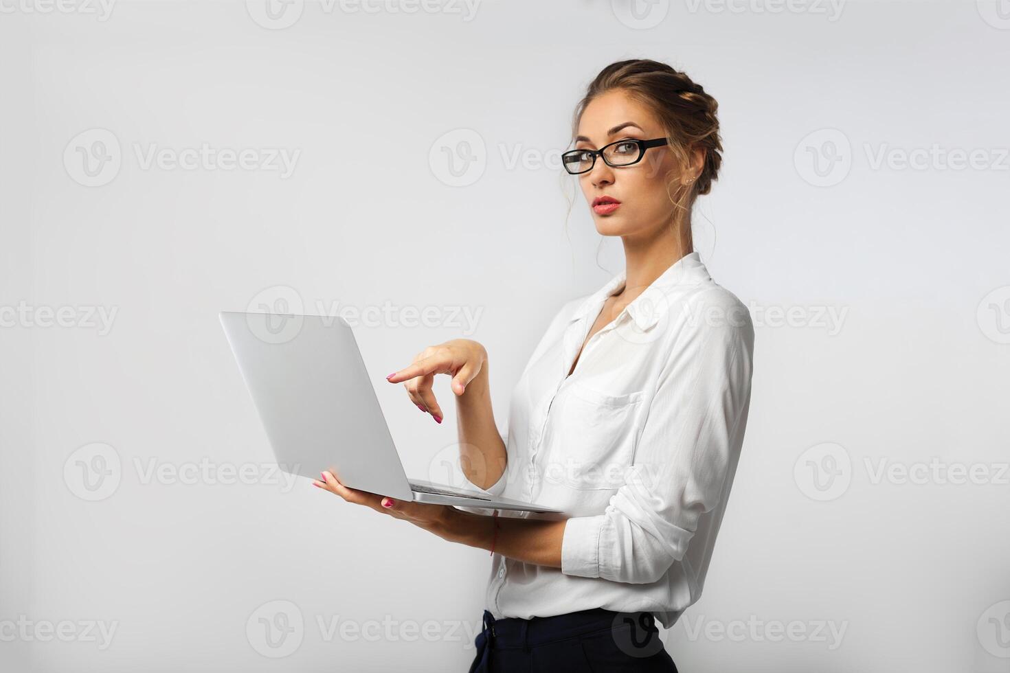 A strict business lady in glasses and co-ordinate office clothes is holding a laptop in her hands and demonstratively pointing at him with her finger photo
