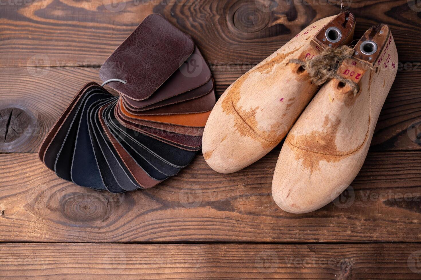 Leather samples for shoes and wooden shoe last on dark wooden table. photo