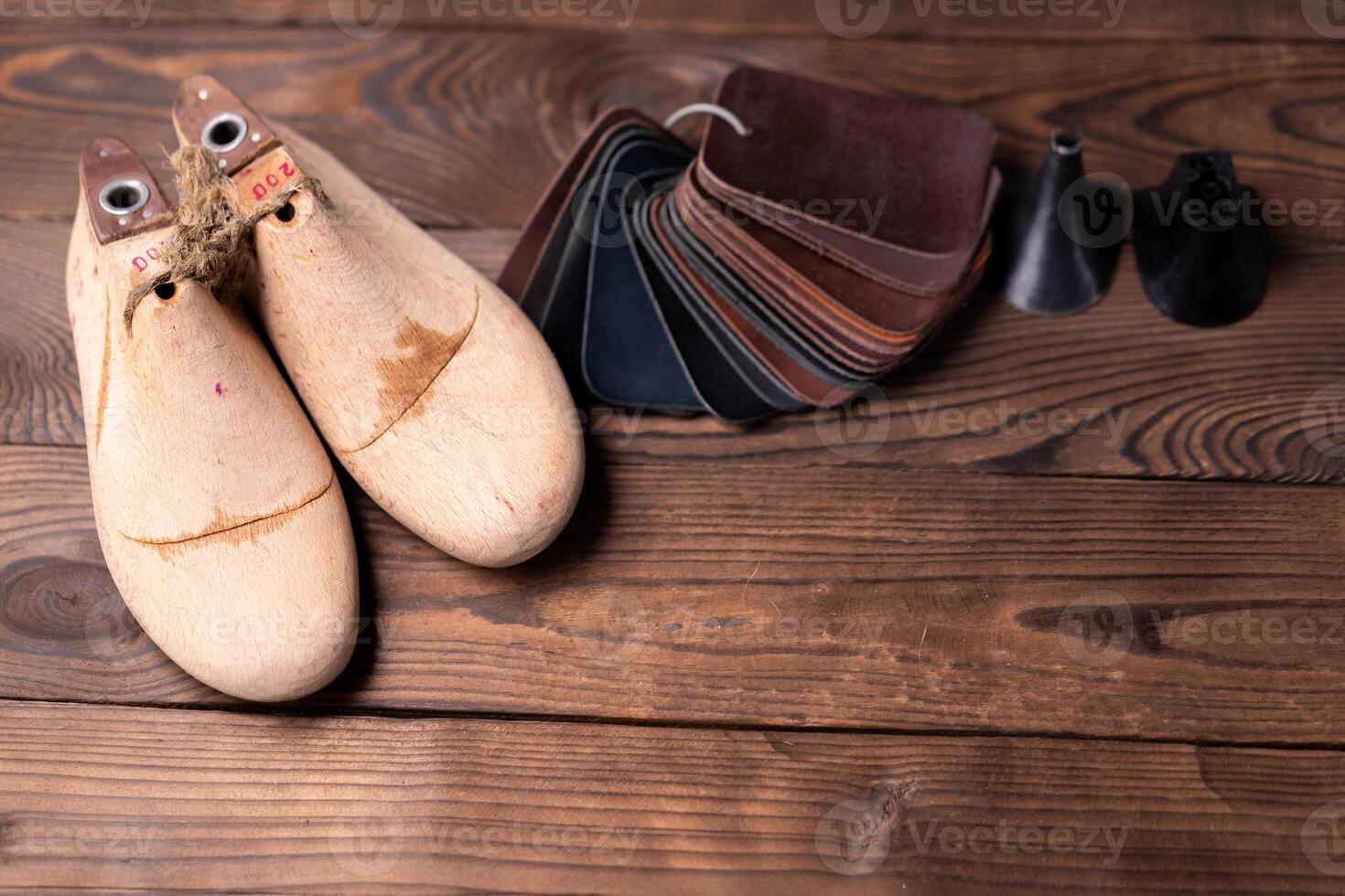 Leather samples for shoes and wooden shoe last on dark wooden table. photo