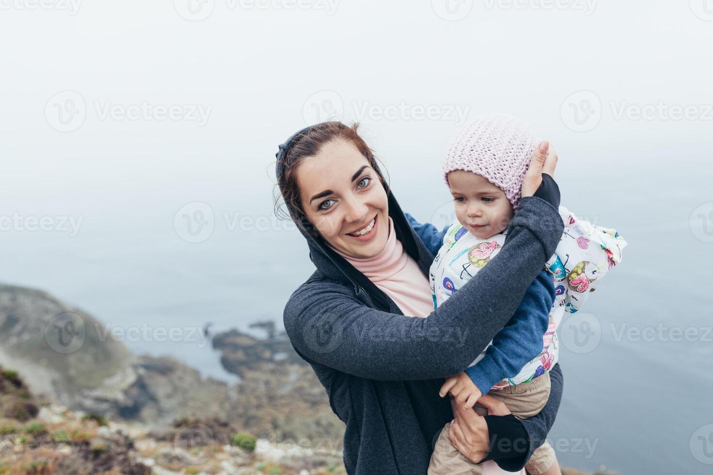 Mother and little daughter standing rock ocean beach autumn season photo