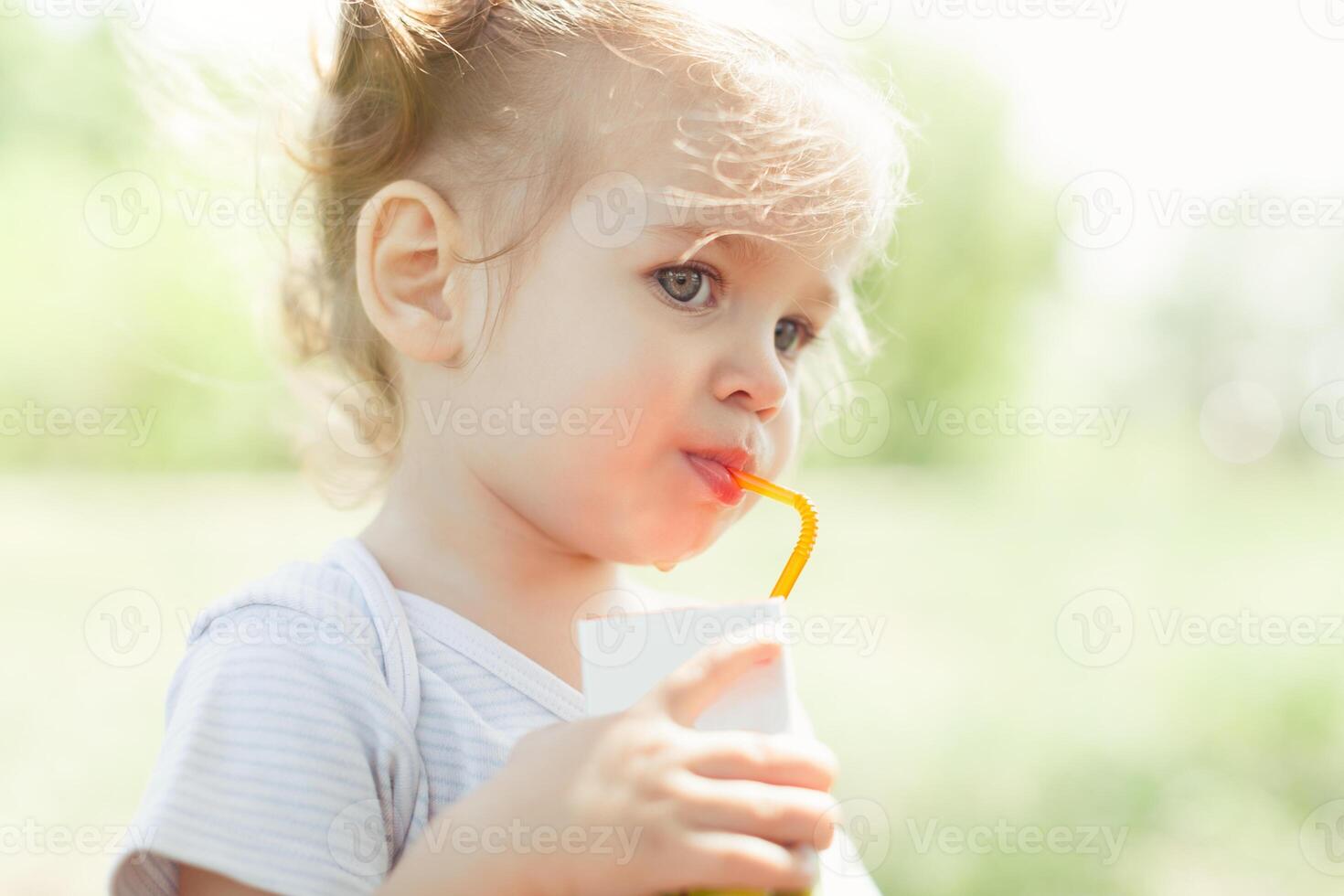 Sunny portrait of a little child drinking from a straw juiceon blurred summer background photo