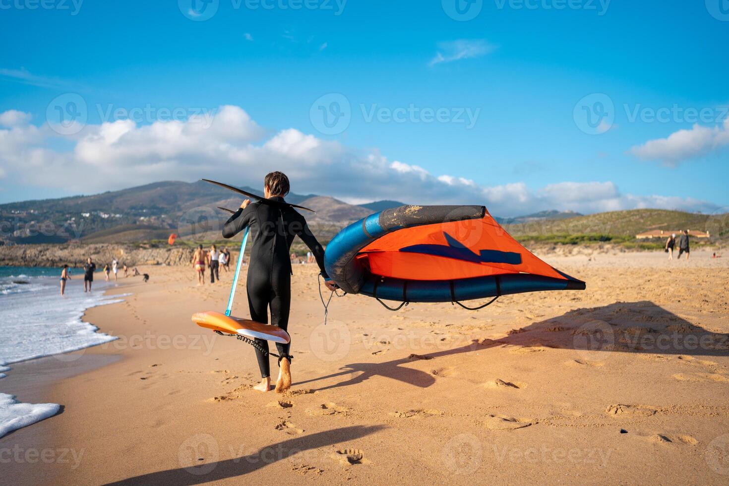 Man with kite hydrofoil equipment walking sandy beach photo