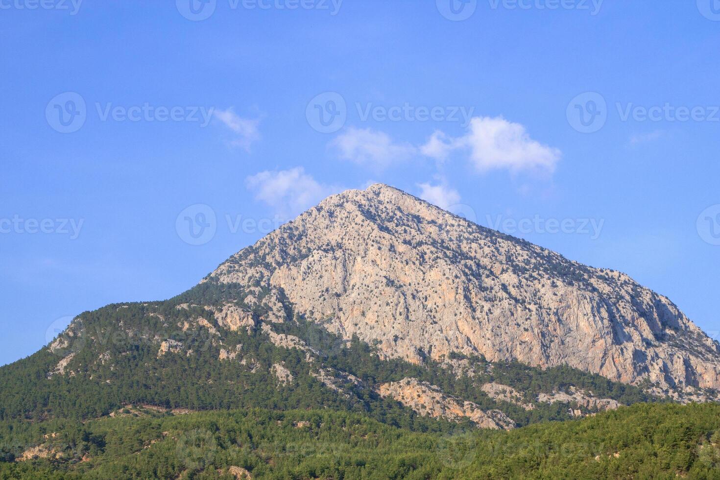 The mountain peeks through the trees against a clear blue sky with white clouds. Doyran Pond, Antalya, Turkey. photo