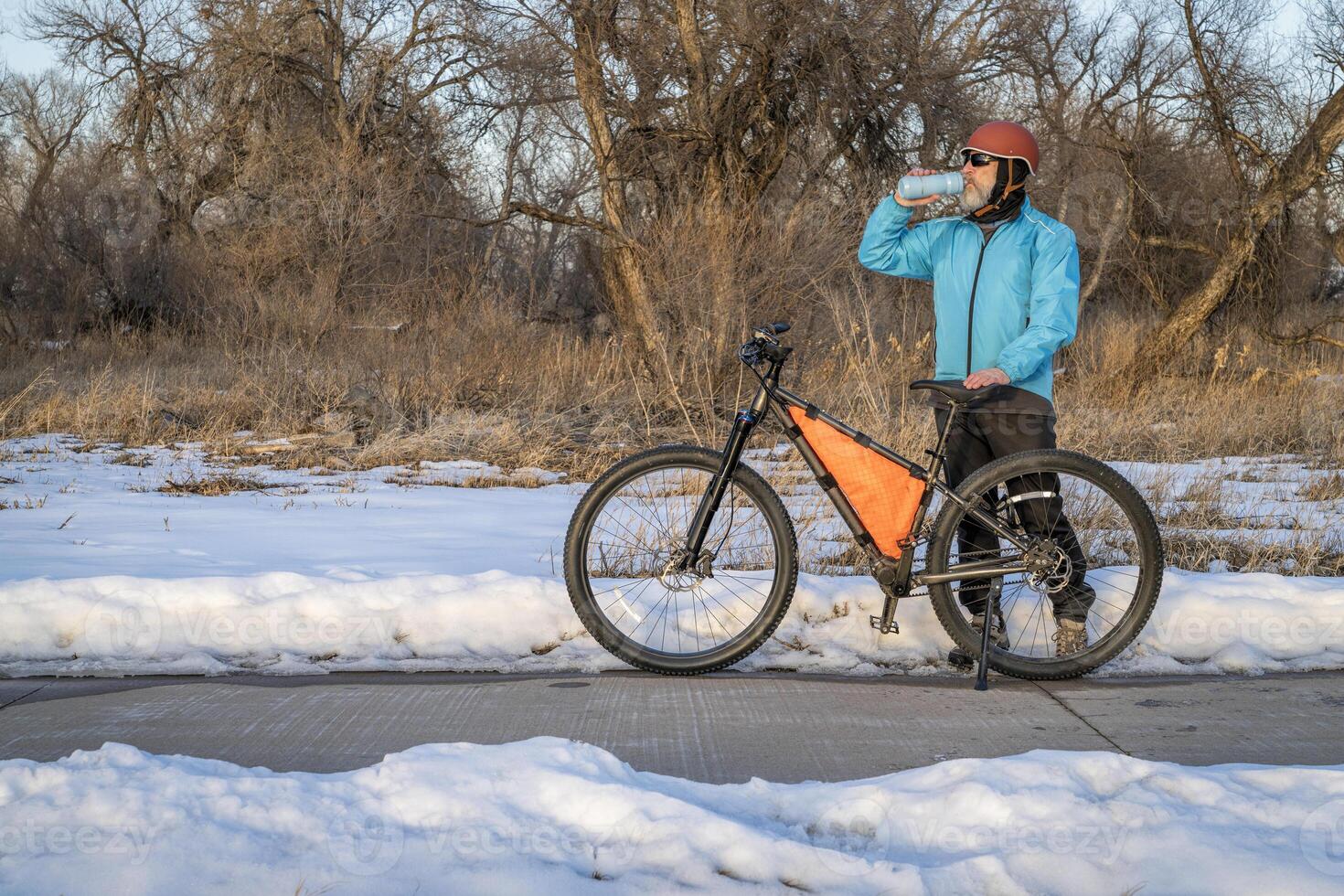 mayor ciclista con un montaña bicicleta es tomando un descanso detener en poudre río sendero cerca greeley, Colorado, en invierno paisaje foto