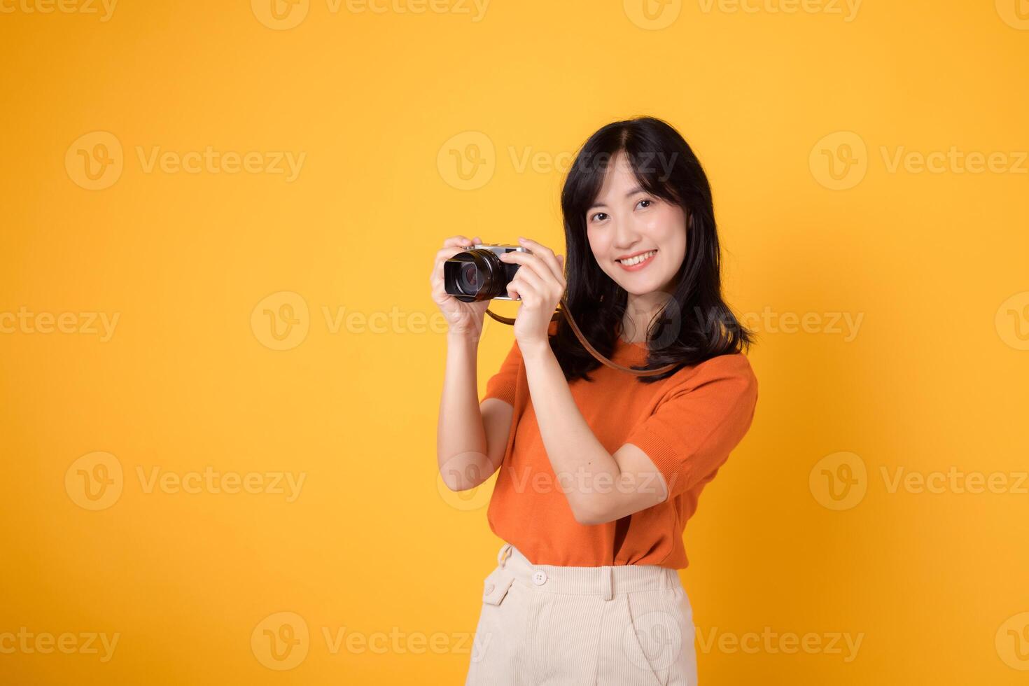 Stylish asian lady traveler with a camera isolated on yellow background, excited for an adventure-filled vacation. photo