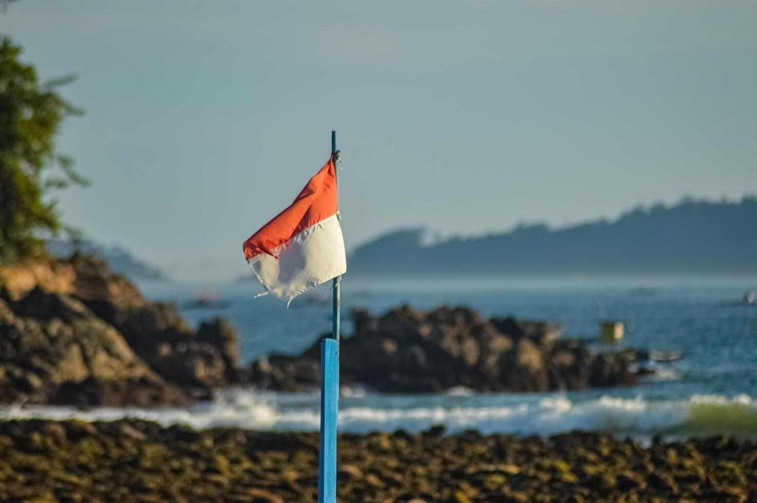 The Indonesian flag fluttering in the wind against the backdrop of a coral rocky beach that looks blurry photo